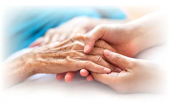 A caregiver holding an elderly patient's hand at home.